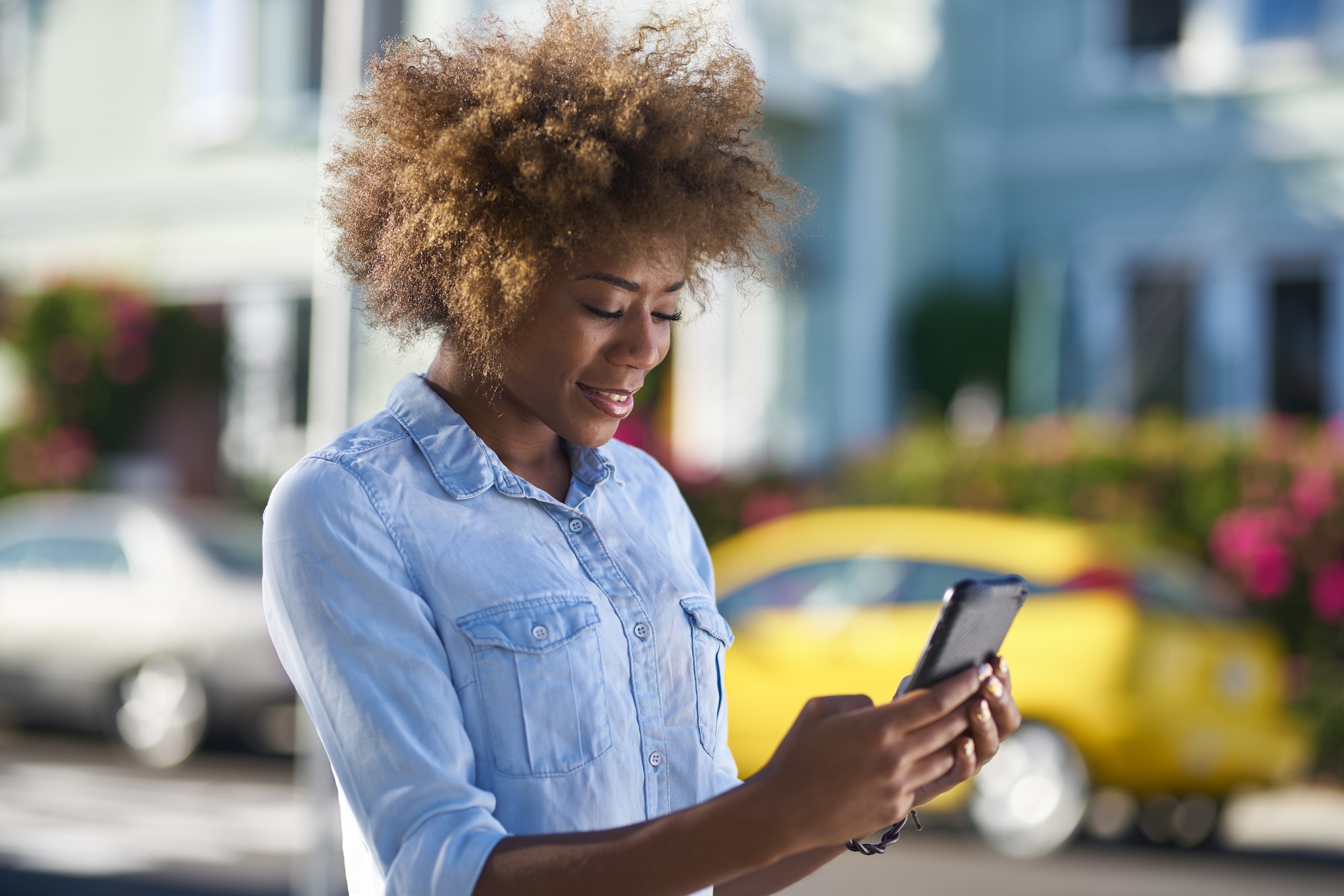 african american woman using smartphone beside street in city